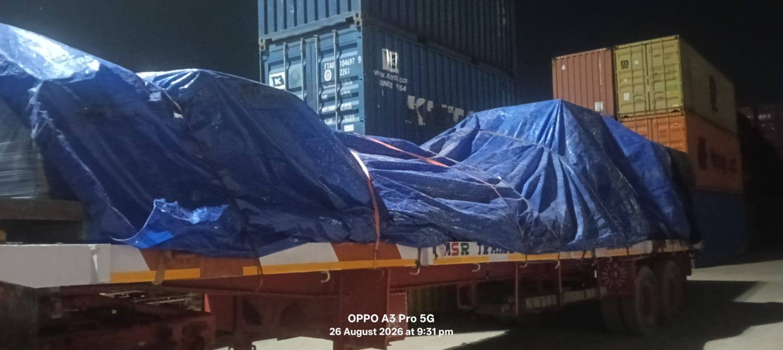 Tarpaulin covered cargo on a flatbed trailer inside a Chennai container yard at night