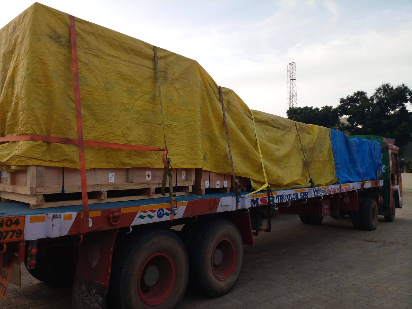 Crated cargo under a yellow tarpaulin, lashed down on an MMM trailer
