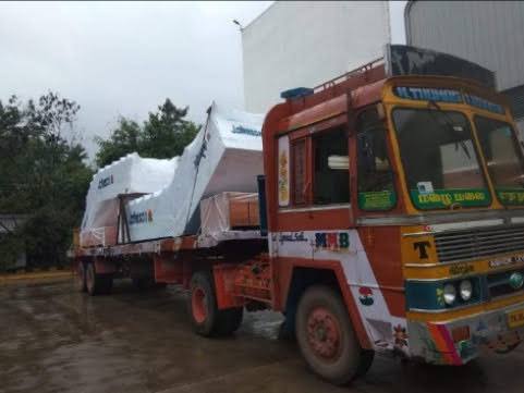 Shrink-wrapped machinery loaded on an MMM flatbed trailer outside a plant